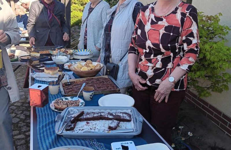 Mitglieder stehen lächelnd hinter einem Tisch mit selbstgebackenem Kuchen