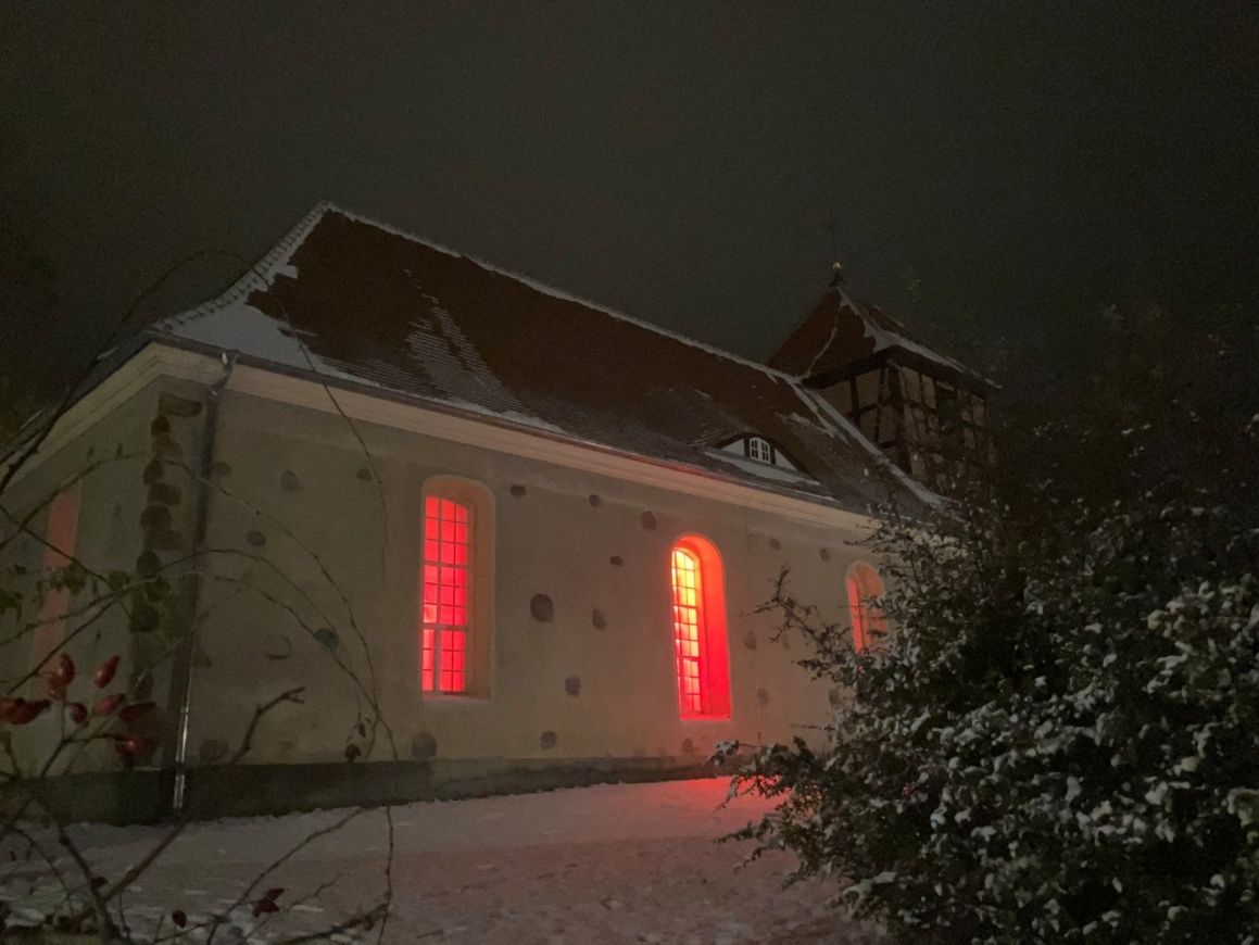 Die Dorfkirche am Abend mit rot leuchtenden Fenstern zum Adventsmarkt