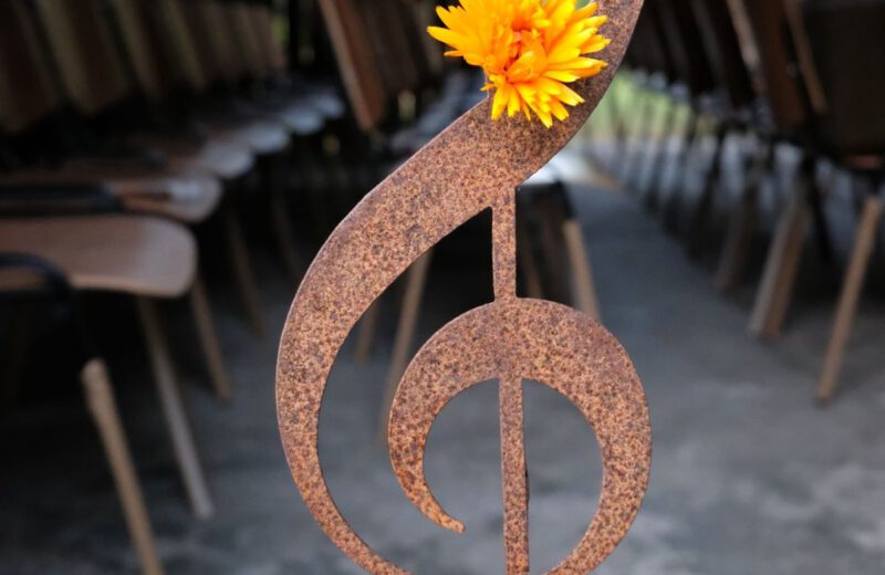 Ein rostiger Notenschlüssel aus Metall mit einer orangefarbenen Blüte